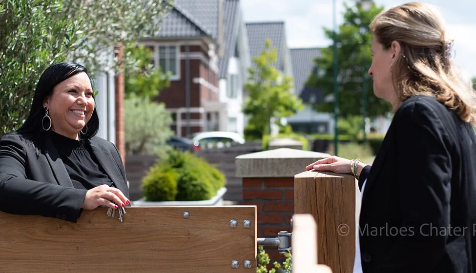 Expat buying agent in the Netherlands handing keys to a client at a wooden gate near a modern residential neighborhood