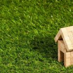 Wooden model house placed on a lush green lawn, symbolizing buying a house in the Netherlands as an expat.