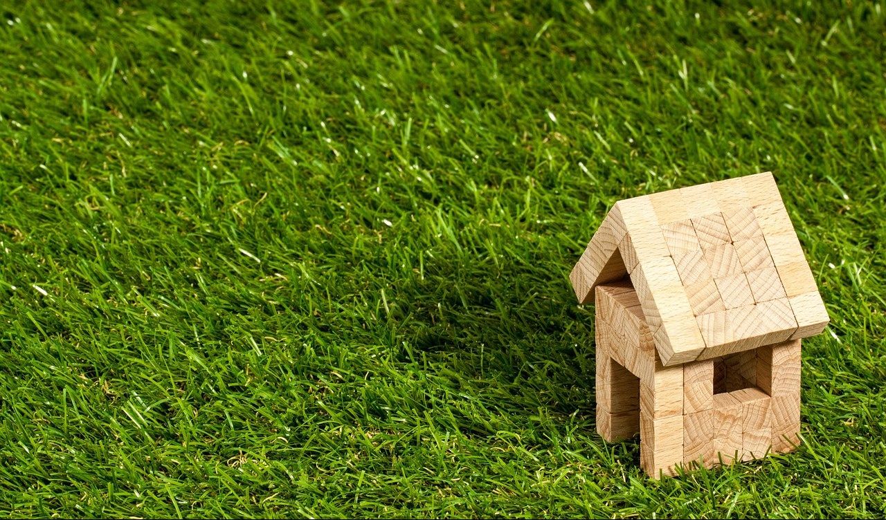 Wooden model house placed on a lush green lawn, symbolizing buying a house in the Netherlands as an expat.